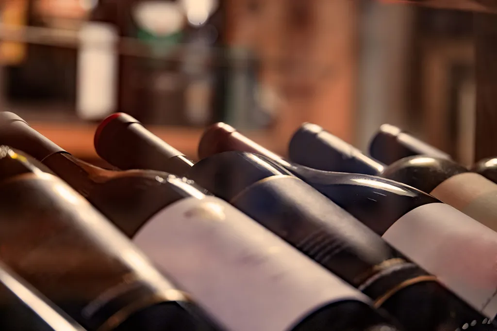 Rangée de bouteilles de vin couchées dans une cave avec un éclairage chaleureux.